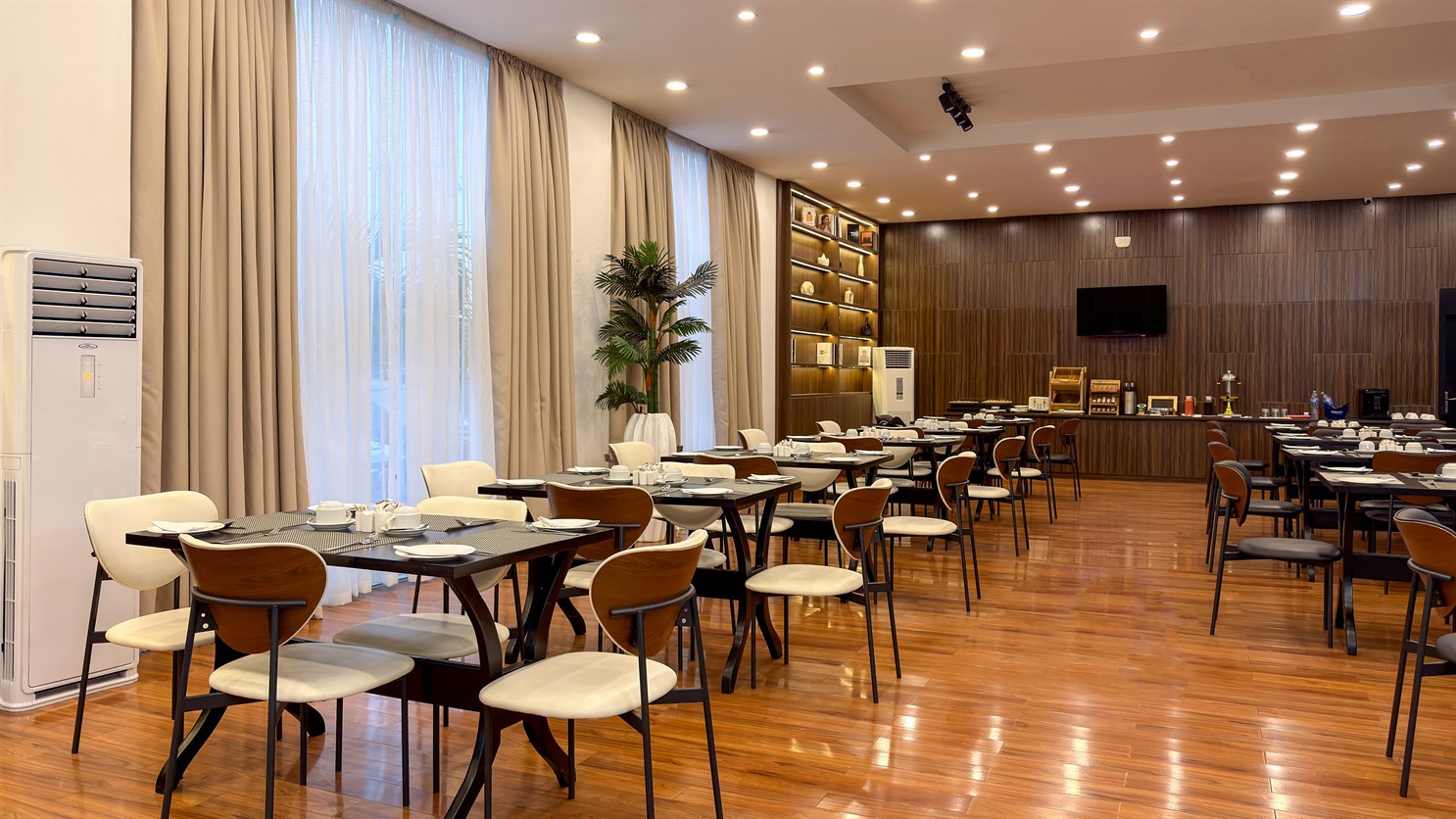 A dining room laid with timber tables and daylight from tall windows