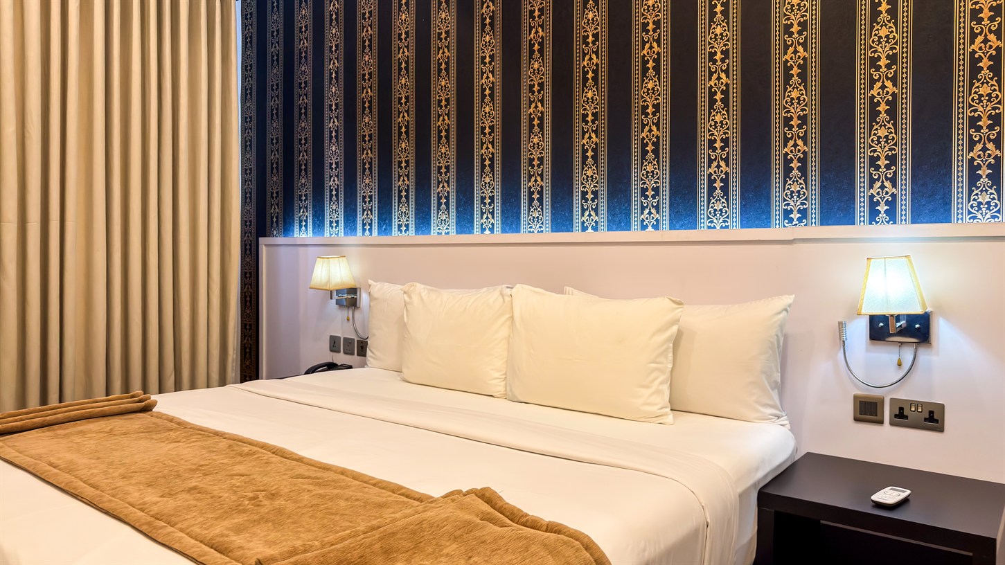 A made bed with cream linen and warm reading lamps against a navy and gold wall